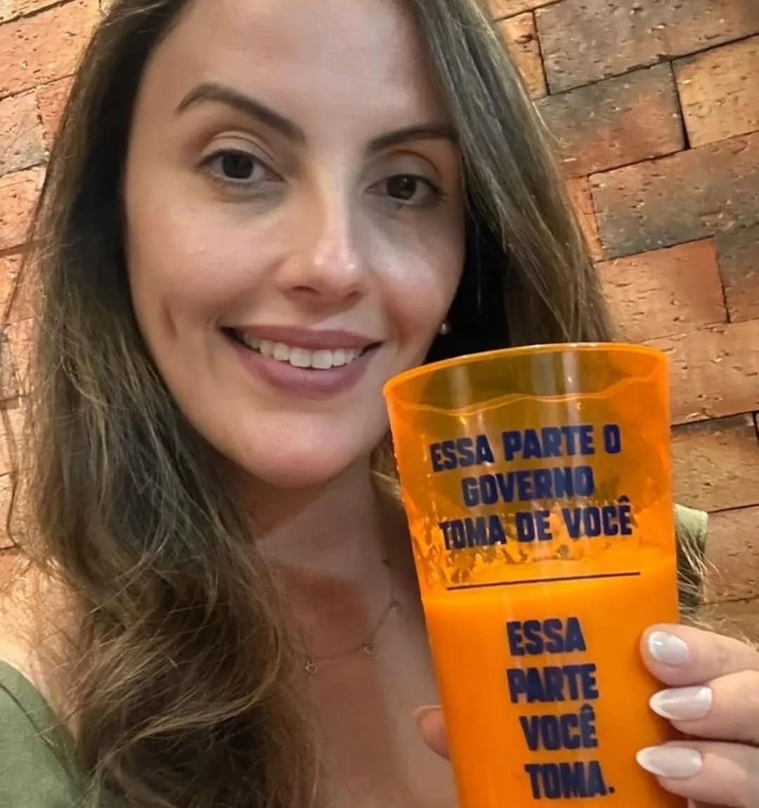 Michele Marques sorrindo e segurando um copo laranja do NOVO